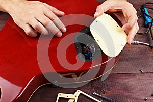 Guitar master opens the cover of electric guitar wiring at workplace