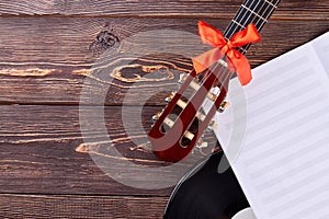 Guitar and music sheets on wooden background.