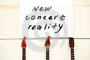 Guitar necks and card with message new concert reality on wooden background.