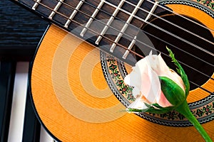 Guitar with pink rose on piano keyboard.