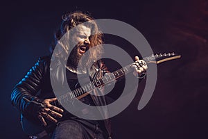 Guitar player. Rockstar bearded man emotional plays on guitar isolated on black background.