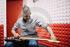 Guitar player setting tone to his music instrument in soundproof studio