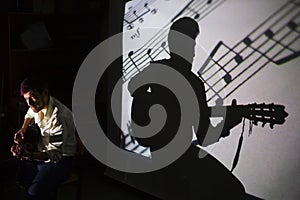 The guitar player is singing the song with a shadow of notes and silhouette of the guitarist on the background