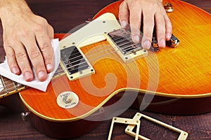 Guitar repairman wipes varnished surface of electric guitar with rag at workplace