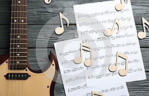 Guitar and sheets with music notes on wooden background
