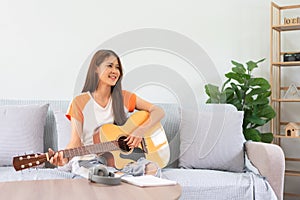 Guitar and singer concept, Young asian woman sitting on couch to playing music with acoustic guitar