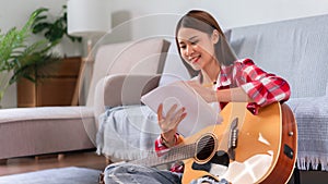 Guitar and singer concept, Young woman is composing song while playing acoustic guitar on the floor