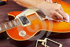 Guitar technician wipes varnished surface of electric guitar with rag at workplace