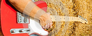 Guitar telecaster in red with a wooden stamp in the hand of a musician background of straw on a sunny summer day