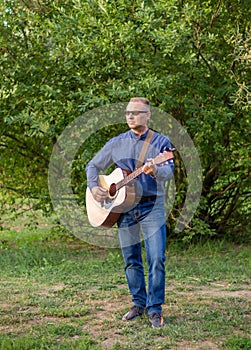 The guitarist of the country singer stands against the sky of the field. Rustic style. Summer vacation.