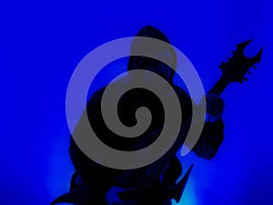 Guitarist with hood and a pointed Heavy Metal guitar with horned headstock on blue background