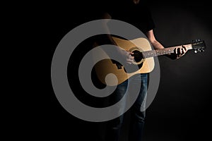 The guitarist in jeans plays an acoustic guitar, on the right side of the frame, on a black background. Horizontal frame