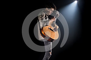 Guitarist, music. A young man plays an acoustic guitar on a black isolated background