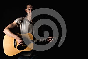 Guitarist, music. A young man plays an acoustic guitar on a black isolated background. Horizontal frame