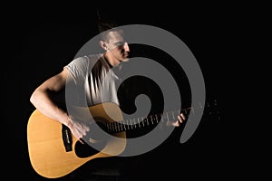 Guitarist, music. A young man plays an acoustic guitar on a black isolated background. Horizontal frame