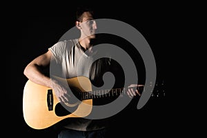 Guitarist, music. A young man plays an acoustic guitar on a black isolated background. Horizontal frame