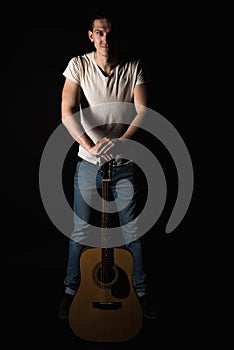 Guitarist, music. A young man stands with an acoustic guitar, on a black isolated background. Vertical frame