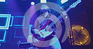 Guitarist performs solo part on electric bass guitar on stage at concert. Blue and yellow light. Slow motion