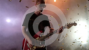 The guitarist performs on stage. Stage light, smoke. From above fall golden confetti