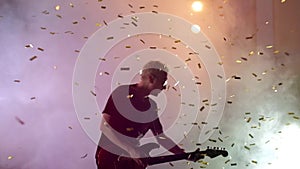 The guitarist performs on stage. Stage light, smoke. From above fall golden confetti