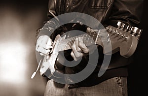 Guitarist player in leather jacket playing a 5 string electric guitar