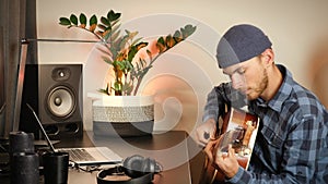Guitarist playing acoustic guitar in cozy living room. Musician plays chords on string music instrument, performs lyric song compo