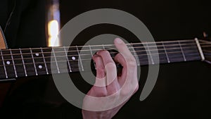 Guitarist playing acoustic guitar in dark room close up.