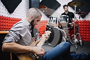 Guitarist playing guitar while sitting on floor in music studio