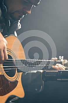 A guitarist plays an acoustic guitar with a microphone on a dark background.