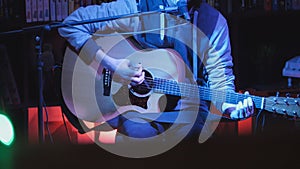 Guitarist plays acoustic guitar and sings microphone in night club, blue lights, close up