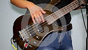 Guitarist plays on a brown bass in studio, dressed in jeans and a black shirt