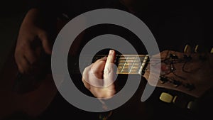 The guitarist plays a classic wooden guitar. Hands of a musician on an acoustic guitar in a dark room.