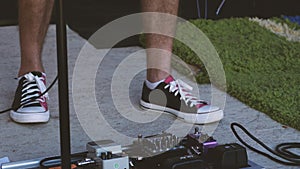 The guitarist`s feet in sneakers against a background of guitar processors, primers, and other electronic devices for the electric