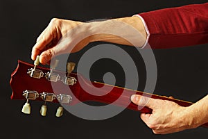 Guitarist tunes the guitar on dark background