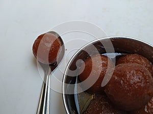 Gulab Jamoon or Jamun in a Steel, Green Color Plastic Cup and Spoon isolated on white Background