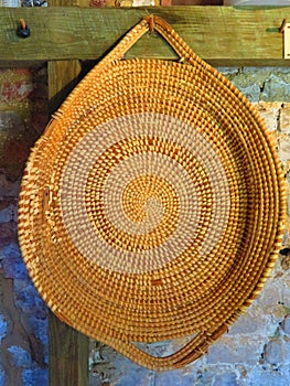 Gullah sweetgrass basket hanging from wooden peg on brick wall