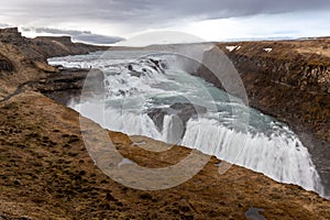 Gullfoss waterfall in Iceland, view of the cascades with water spray, canyon covered with moss, May, spring