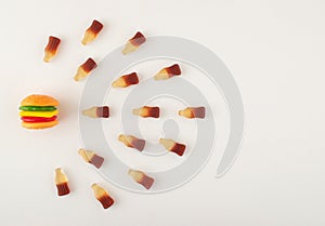 Gummy candies in burger and bottles shape arranged in line on white background. Food compatibility concept