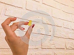 A gummy yellow bear in the hands of a girl with a red manicure. bear are kept on a white brick background. homemade wall with