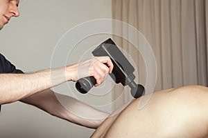 Gun percussion massage back muscle athletic man in medical room