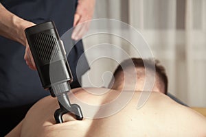 Gun percussion massage back muscle athletic man in medical room