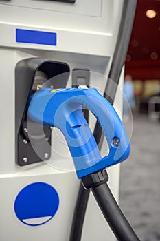 Gun with a powerful cable for charging an electric vehicle is inserted into the socket of the charging station column while