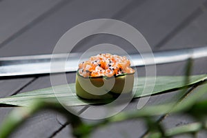 Gunkan Sake Green sushi on bamboo leaf near Japanese knife with green plant on foreground.