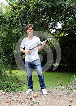 The gunner man holding long gun in hands and turned left sideways with white shirt and denim jean.