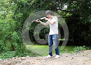 The gunner man standing long gun aiming right sideways with white shirt and denim jean.