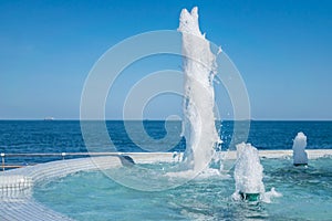 The gush of water of fountain. Splash and Foam of water. Blue vertical fountain with mosaic pool on the wooden terrace, by the se
