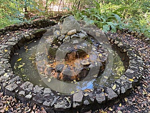 gushing spring built of stones in autumn park with colorful trees and bushes