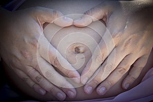 Gut of seven months pregnant woman making a heart with her hands