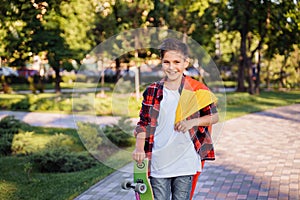 Guy of 9 years old riding skateboard on sunny road in the evening in the city park. Holding fluttering flag of Germany. Happy