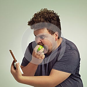 Guy, apple and chocolate in studio with choice of junk food, sweet or diet for wellness. Plus size, male person eating